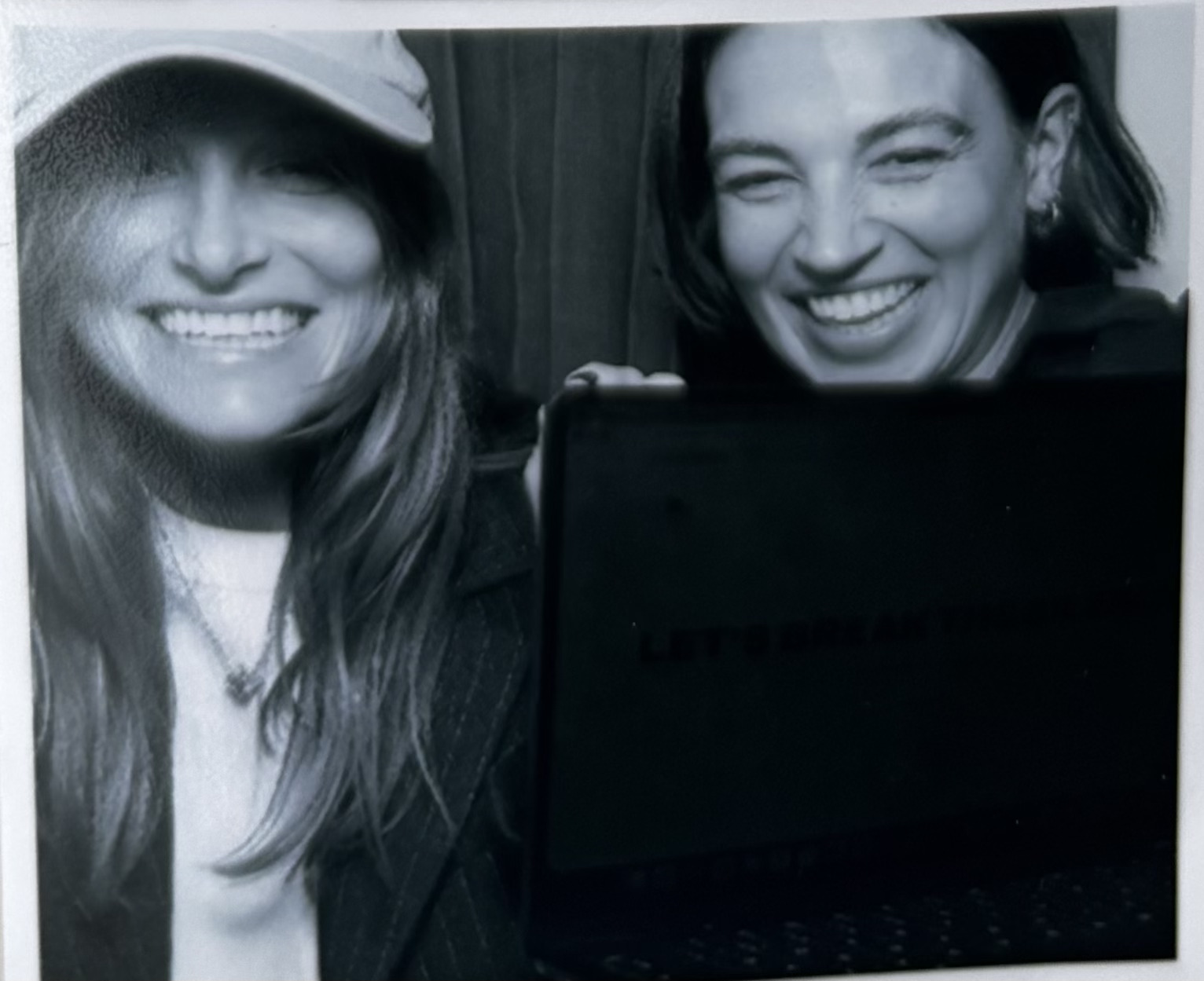 Cécile and Julia grinning behind a laptop in a black-and-white photobooth picture